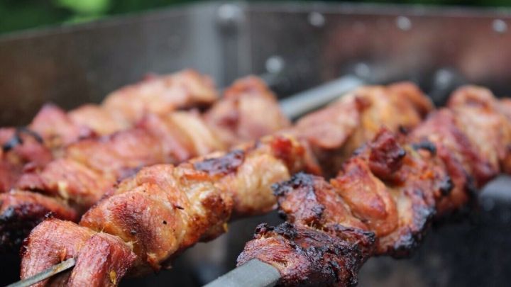 Gegrillte Schaschlik-Spie&szlig;e brutzeln auf dem Grill und verbreiten k&ouml;stliches Aroma in einer gr&uuml;nen Umgebung.