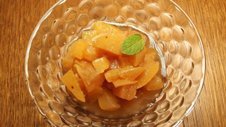 Karamellisierte Apfelst&uuml;cke liegen in einer eleganten Glasschale, verziert mit einem Minzblatt, auf einem Holztisch.