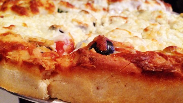 Eine k&ouml;stliche Pizza nach Art des Hauses steht auf einem Teller, frisch aus dem Ofen, mit knusprigem Rand und geschmolzenem K&auml;se.