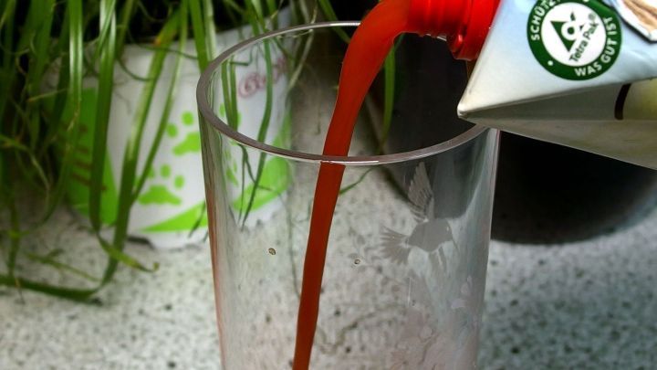 Ein roter Tomatensaft wird aus einer Verpackung in ein hohes Glas gegossen, um Kater-Symptome zu lindern.