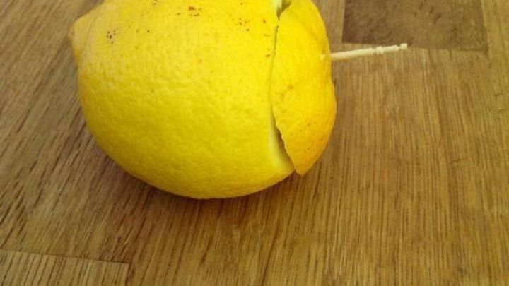 Eine Zitrone steht auf einem Holztisch, w&auml;hrend ein kleiner Holzstab aus ihrer Seite ragt, was ihr ein einzigartiges Aussehen verleiht.