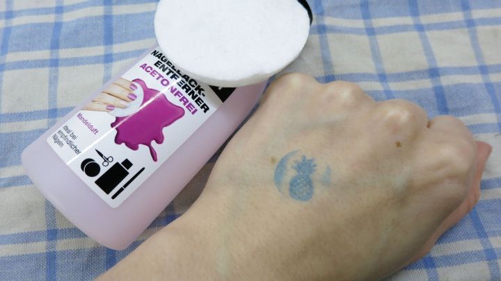 Eine Flasche Nagellackentferner steht neben einer Hand mit einem Disco-Stempel-Abdruck auf einem karierten Tuch.