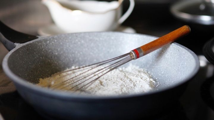 In einer Pfanne wird mit einem Schneebesen eine Mehlschwitze anger&uuml;hrt, w&auml;hrend im Hintergrund eine Sauciere steht.