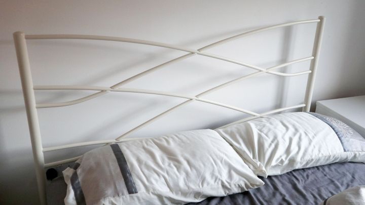 Ein Bett mit einem wei&szlig;en Kopfteil liegt in einem modernen Schlafzimmer. Die Kissen sind ordentlich platziert, w&auml;hrend alles ruhig wirkt.