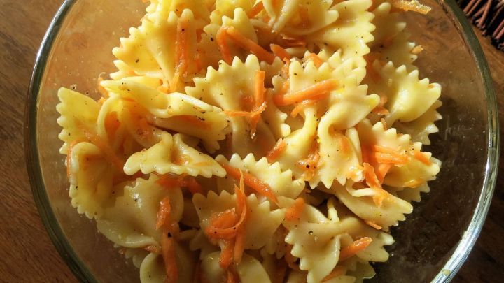 Ein Salat aus Nudeln und M&ouml;hren in einer Glas-Sch&uuml;ssel, appetitlich angerichtet und auf einem Holzuntergrund platziert.