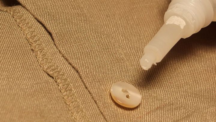 Ein Knopf liegt auf einem beigen Hemd, w&auml;hrend eine Kleberflasche ihn fixiert, um Verlust zu verhindern.