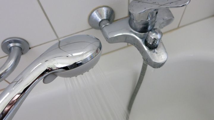 Ein Duschkopf gibt sanft Wasser ab, w&auml;hrend er an einem gl&auml;nzenden Wasserhahn in einem modernen Badezimmer angebracht ist.