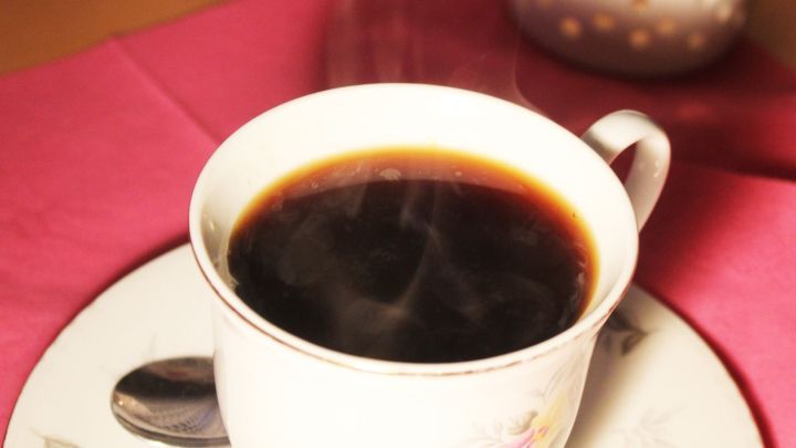 Eine dampfende Tasse Kaffee steht auf einem Teller, umgeben von einer pinken Tischdecke.