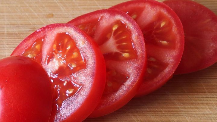 Schnittfeste Tomaten sind gleichm&auml;&szlig;ig in Scheiben geschnitten und liegen auf einem Holzbrett. Es handelt sich um frische, rote Tomaten.