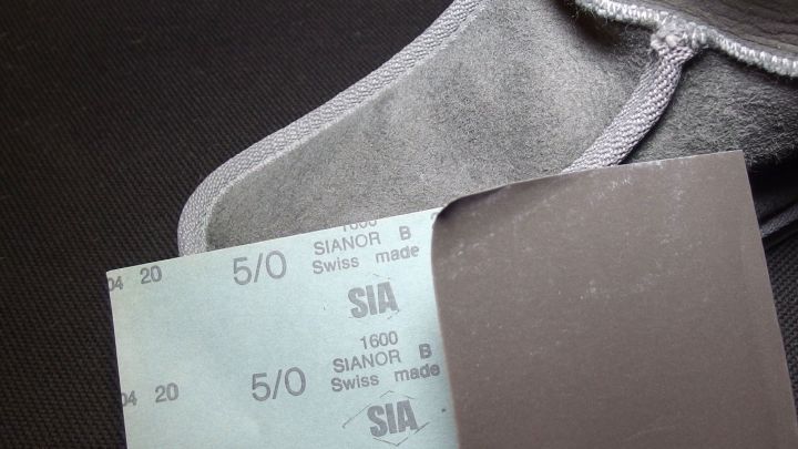 Wildlederschuhe liegen neben einem St&uuml;ck Sandpapier, das zum Entfernen von Wasserflecken genutzt wird.