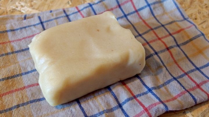 Ein St&uuml;ck Marzipan liegt auf einem karierten K&uuml;chentuch, bereit zur Lagerung, um seine Frische zu bewahren.