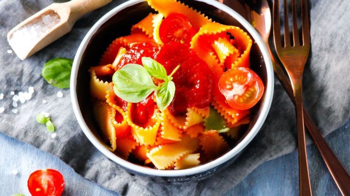 Eine Sch&uuml;ssel mit bunten Nudeln in Tomatenso&szlig;e, garniert mit frischem Basilikum, auf einem Tisch mit Besteck.