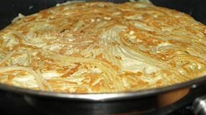 Ein goldbraunes Spaghetti-Omelett br&auml;t in einer Pfanne, wo die Pasta gleichm&auml;&szlig;ig verteilt ist und eine knusprige Kruste bildet.