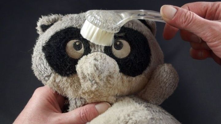 Ein verfilztes Kuscheltier wird mit einer B&uuml;rste gepflegt, w&auml;hrend H&auml;nde z&auml;rtlich das Spielzeug festhalten.