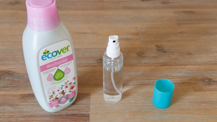 Eine Flasche Weichsp&uuml;ler steht neben einer leeren Spr&uuml;hflasche auf einem Holztisch, bereit zur Herstellung eines g&uuml;nstigen Raumsprays.