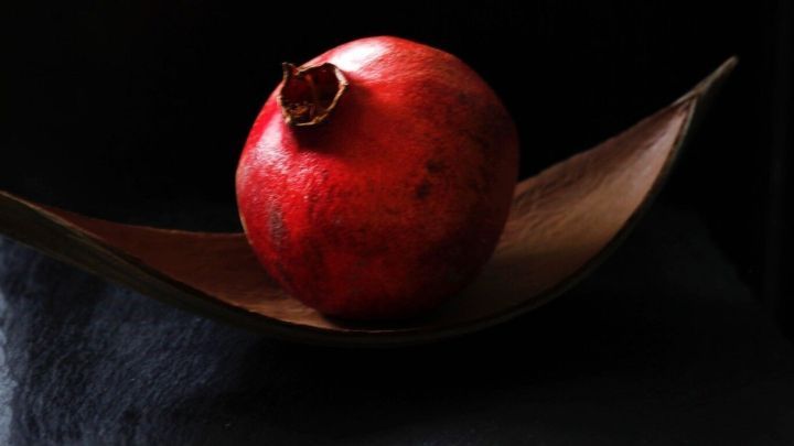 Ein Granatapfel liegt auf einer eleganten, gebogenen Holzschale vor einem dunklen Hintergrund und strahlt Frische aus.