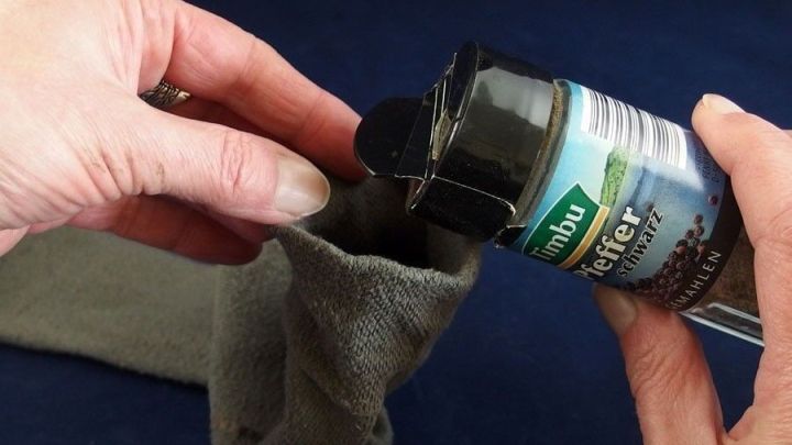 Eine Hand f&uuml;llt Pfeffer in einen grauen Socken, um warme F&uuml;&szlig;e zu bekommen. Der Hintergrund ist dunkelblau.