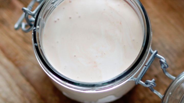 Ein Glas mit selbstgemachtem Joghurt steht auf einer Holzoberfl&auml;che, das Joghurt ist cremig und frisch.