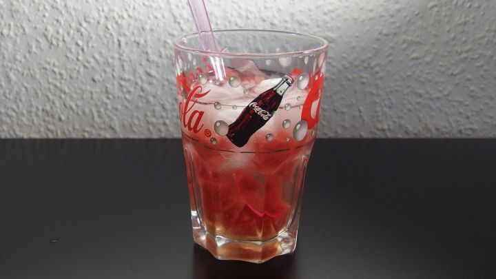 Ein Glas mit einem erfrischenden Wassermelonen-Drink, gef&uuml;llt mit Eisw&uuml;rfeln, steht auf einem schwarzen Tisch.