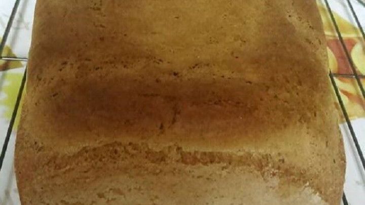 Ein goldbraunes Mischbrot ohne Sauerteig liegt auf einem Kuchengitter in einer K&uuml;che mit buntem Tischw&auml;sche.