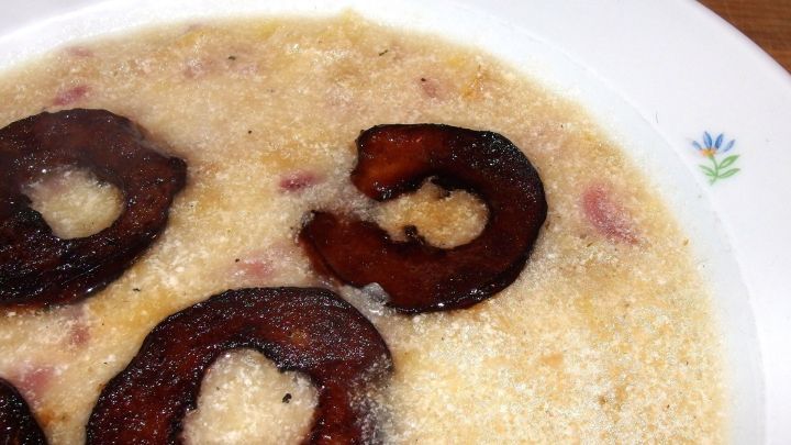 Ein Teller mit Apfelsuppe, die mit braun gebratenen Apfelscheiben garniert ist, liegt auf einem Holztisch.