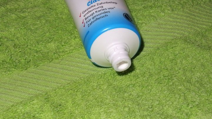 Eine Tube Zahnpasta liegt auf einem gr&uuml;nen Handtuch, bereit, um Klebstoffreste von Fingern&auml;geln zu entfernen.