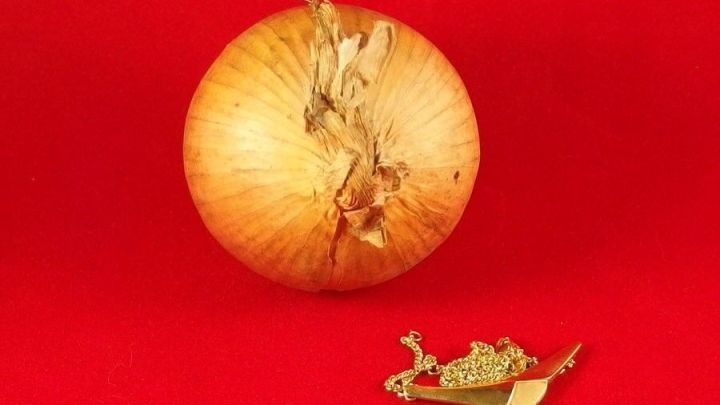 Goldschmuck liegt gl&auml;nzend neben einer Zwiebel auf rotem Hintergrund.