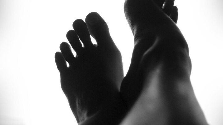 Glatte Beine sind sichtbar, w&auml;hrend sie entspannt liegen; der Lichtkontrast hebt die Haut sanft hervor.