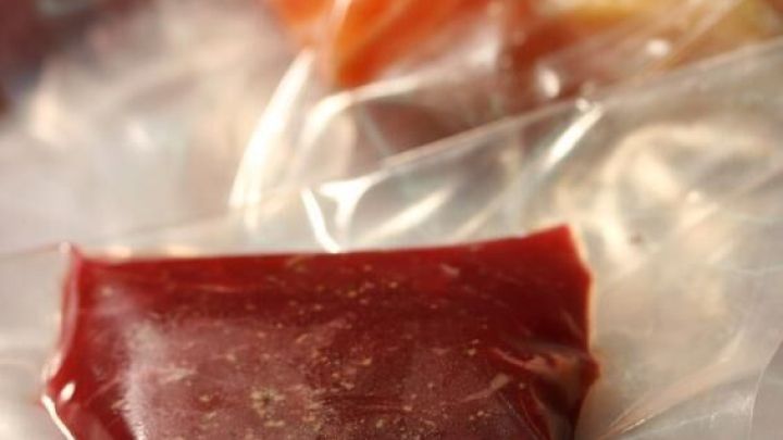 Vakuumverpackte Lebensmittel liegen auf einem Tisch, darunter rotes Fleisch und Lachs, bereit zur Lagerung oder Zubereitung.