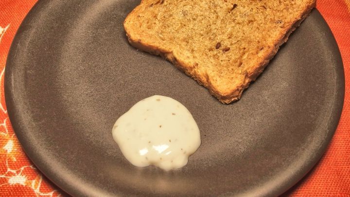 Ein knuspriges St&uuml;ck Brot liegt auf einem grauen Teller neben einem Klecks Knoblauchdip, alles auf einem roten Tisch.
