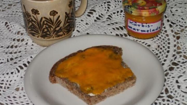 Auf einem Teller liegt ein St&uuml;ck Brot mit K&uuml;rbismarmelade, daneben eine Tasse Kaffee und ein Glas Marmelade.