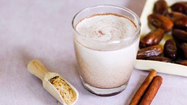 Ein Glas Reis-Soja-Drink mit Datteln steht auf einem Tisch, umgeben von weiteren Datteln und Zimtstangen.