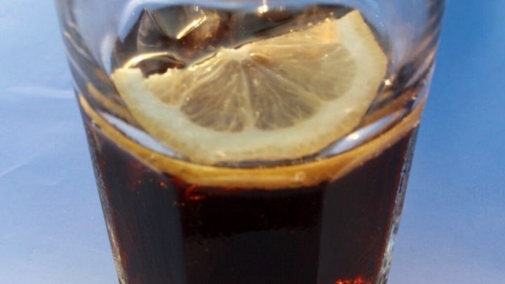 Ein Glas Cola mit einer Zitronenscheibe steht auf einem Tisch in der Sonne und vermittelt ein erfrischendes Gefühl.