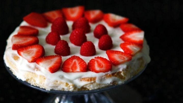 Eine bunte Tortenschicht mit frischen Erdbeeren und Himbeeren, dekoriert auf einem eleganten Teller, vor dunklem Hintergrund.