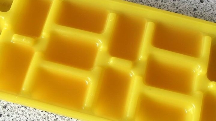 Eine gelbe Eisw&uuml;rfelform liegt auf einer Arbeitsfl&auml;che und enth&auml;lt frisch gepressten Zitronensaft zur Herstellung von Eisw&uuml;rfeln.