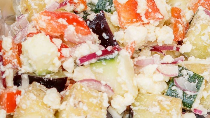 Ein bunter Gem&uuml;sesalat mit Feta und Zwiebeln, angerichtet in silberner Folie, bildet ein frisches, cremiges Ensemble.