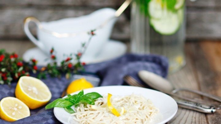 Eine Schale mit Spaghetti in Zitronensauce steht auf einem rustikalen Tisch, umgeben von frischen Zitronen und Kr&auml;utern.