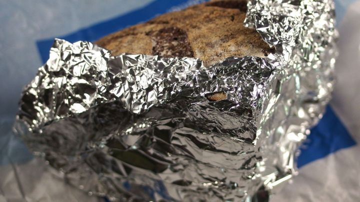 Ein St&uuml;ck angeschnittenes Brot ist in Alufolie eingewickelt, um seine Frische zu bewahren, auf einem blauen Hintergrund.