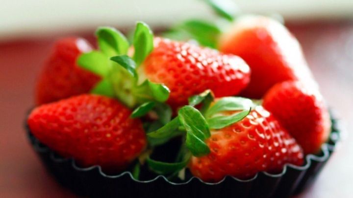 Frische, rote Erdbeeren liegen in einer schwarzen Schale auf einem Tisch, bereit f&uuml;r ein k&ouml;stliches Balsamico-Dessert.