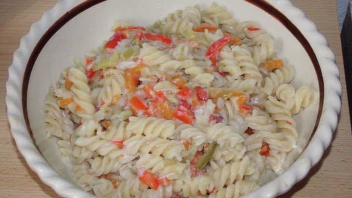 Ein bunter Nudelsalat liegt in einer wei&szlig;en Schale, frisch zubereitet und bereit zum Servieren.