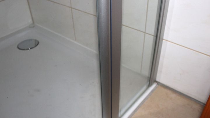 Eine gl&auml;serne Duschkabine zeigt hartn&auml;ckige Kalkflecken, w&auml;hrend sie in einem sauberen Badezimmer steht.