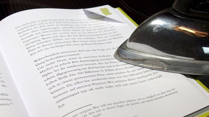 Ein offenes Buch liegt auf einem Tisch, w&auml;hrend ein Dampfb&uuml;geleisen &uuml;ber die Seiten gleitet, um Knicke zu entfernen.