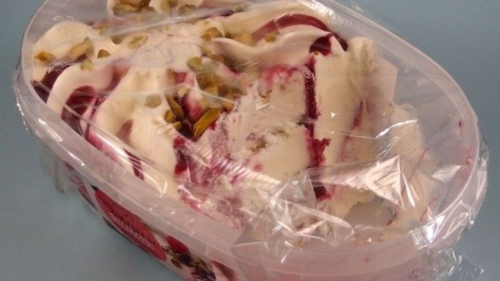 Eine Plastikkuegel mit Eis ist teilweise ge&ouml;ffnet und zeigt fluffiges Eis mit Kirsch- und Nussst&uuml;ckchen im Inneren.