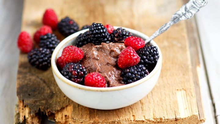 Eine Sch&uuml;ssel Mousse au Chocolat wird mit frischen Himbeeren und Brombeeren auf einem Holzbrett pr&auml;sentiert.