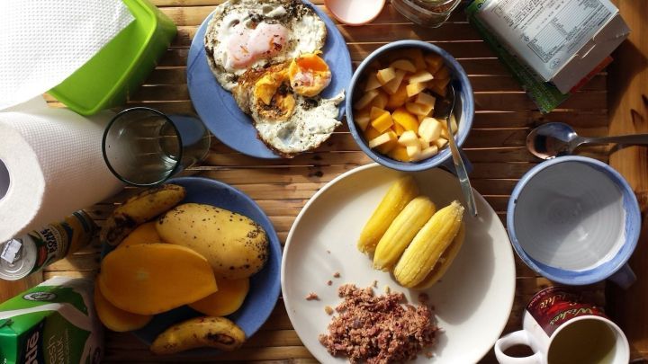 Ein Tisch ist gedeckt mit verschiedenen Gerichten, darunter Eier, Obst und Bananen, die zum Urlaub zu Hause einladen.