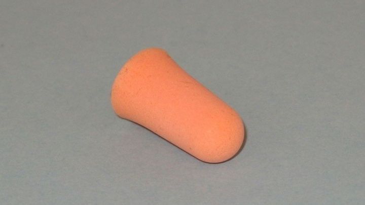 Ein orangefarbener Ohrenst&ouml;psel liegt auf einem grauen Hintergrund, bereit zur richtigen Platzierung im Ohr f&uuml;r Ruhe.