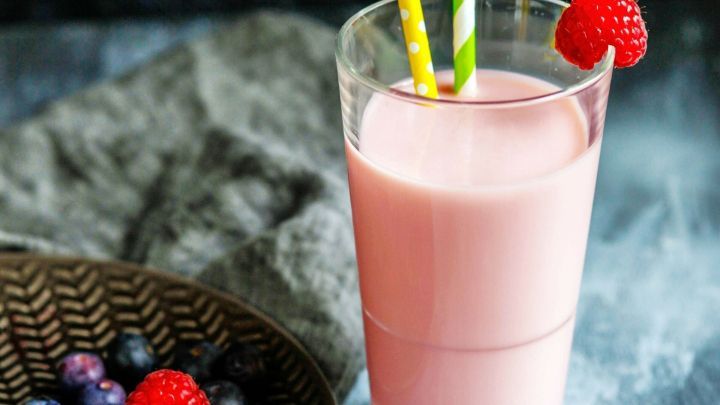 Ein frischer Fruchtmix wird in einem Glas serviert, dekoriert mit Himbeeren und bunten Strohhalmen, umgeben von Beeren.
