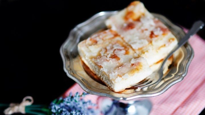 Ein Zuckerkuchen liegt auf einem silbernen Teller, umgeben von einer rosa Serviette und einer blauen Blume.