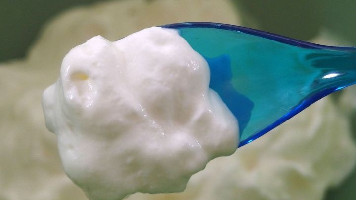 Ein L&ouml;ffel mit steifer Sahne zeigt die cremige Textur, w&auml;hrend der Hintergrund eine Sch&uuml;ssel mit weiterer Sahne erahnen l&auml;sst.