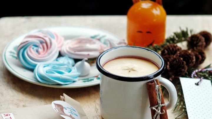 Ein Keramikbecher mit Kinderpunsch steht auf einem Tisch, umgeben von bunten S&uuml;&szlig;igkeiten und festlicher Dekoration.
